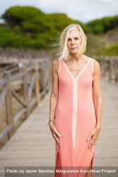 Austere older woman with grey hair on wooden walkway near the coast, vertical 4mzXNb