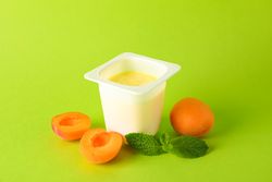 Plastic cup with yogurt and fruits on color background, space for text