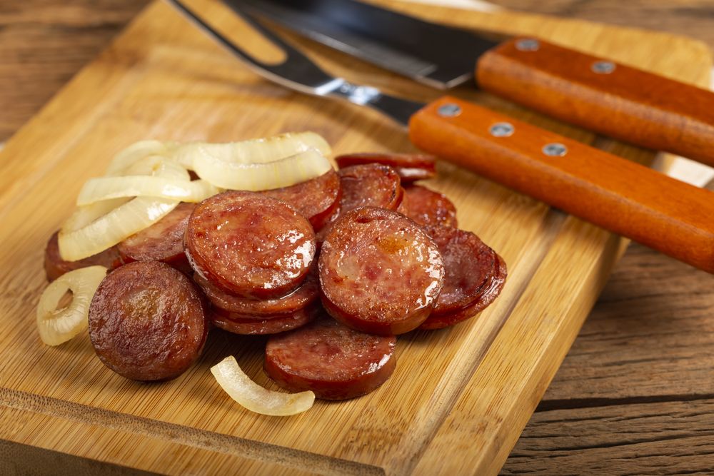 Sliced calabrese sausage with onion on wooden background.
