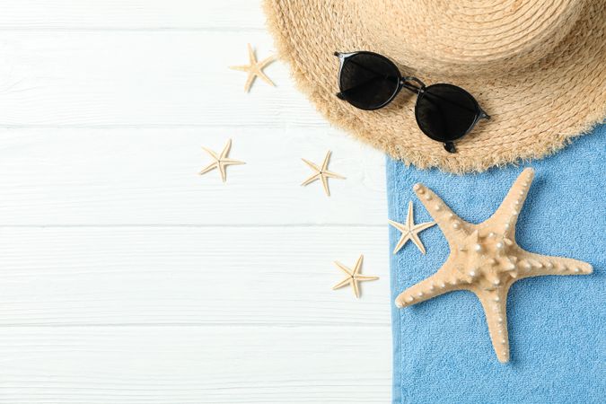 Straw hat, sunglasses, towel and starfishes on wooden background, space for text and top view. Summer vacation backdrop