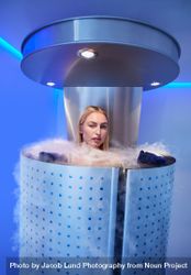 Blonde woman in cryotherapy chamber with steam coming out over the top 4jVGor