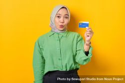 Surprised Muslim woman in headscarf and green blouse holding credit card 4B91e5