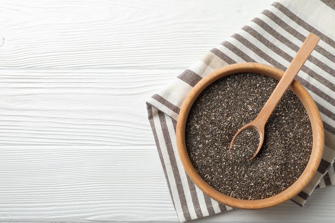 Wooden bowl with chia and spoon on wooden background, top view