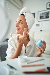 Cheerful female applying cream on face