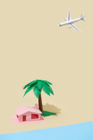 Palm tree, airplane and pink house made of paper on beige background