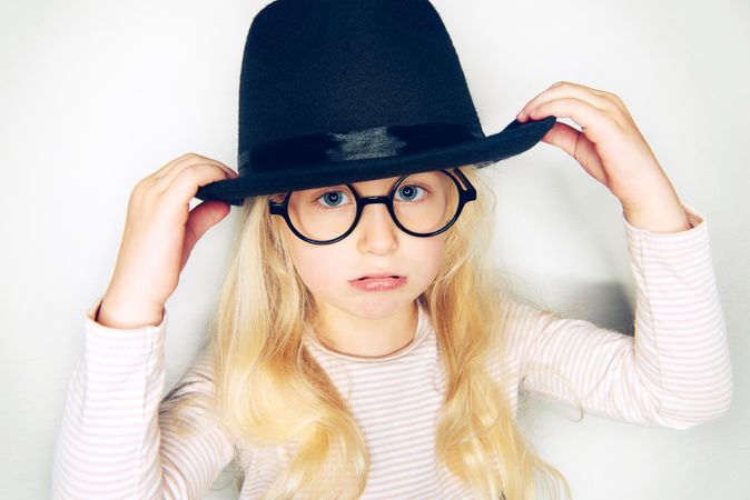 Pouting blonde girl with pursed lips wearing hat and glasses with her arms up