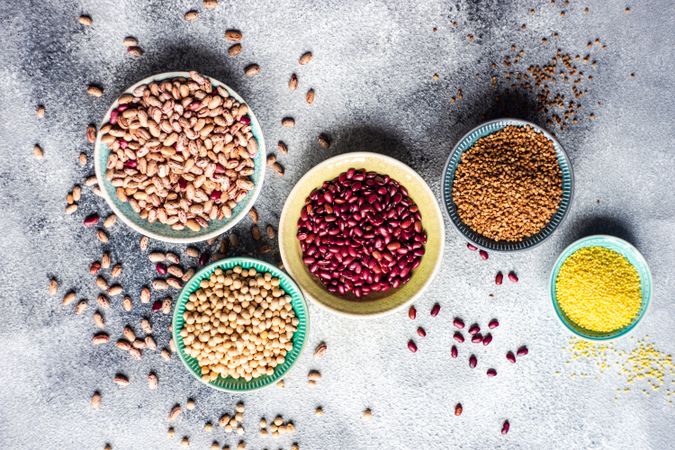 Bowls of dried grains and legumes from pantry on grey counter with copy space