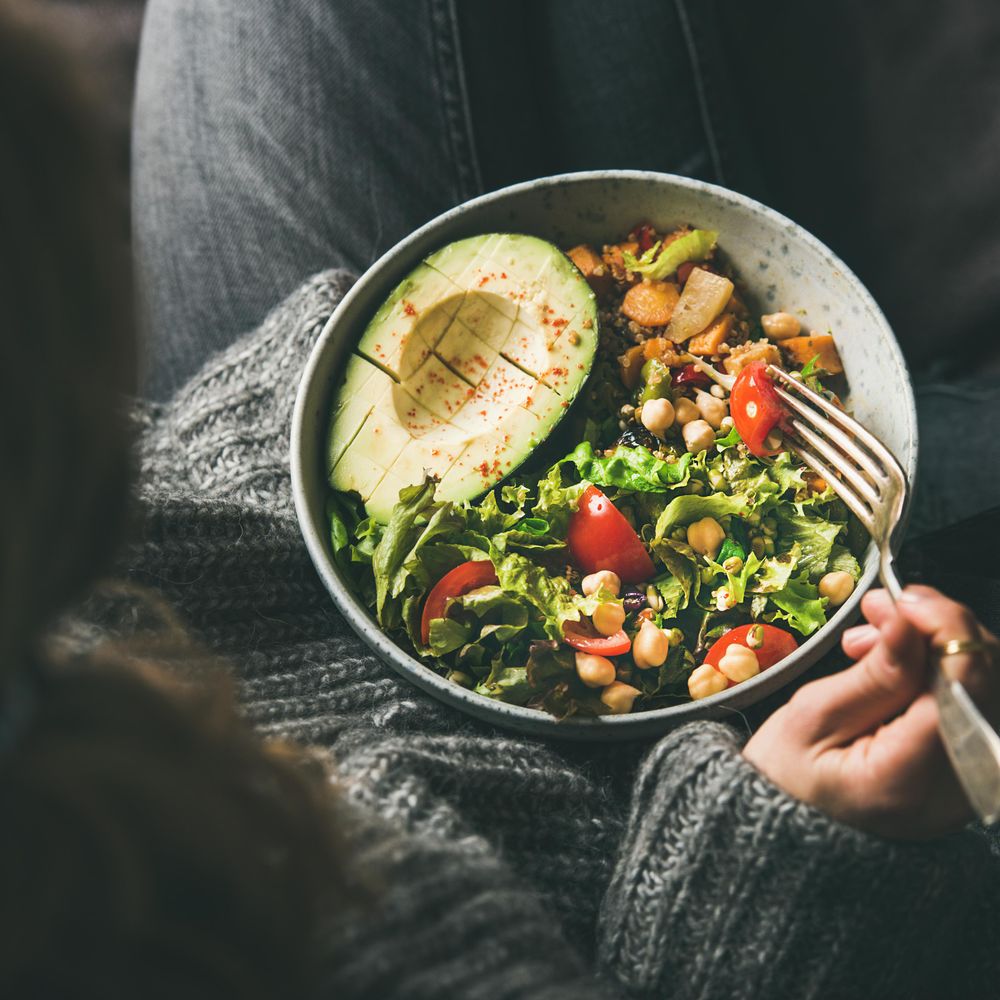 Woman in jeans and sweater eating bowl of fresh salad, top view, square crop