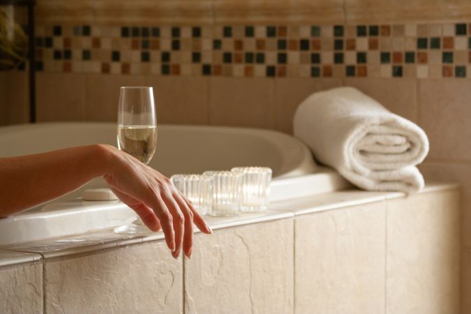 Woman Relaxing in the Bathroom Spa Tub with a Glass of Sparkling Champagne and Candles.