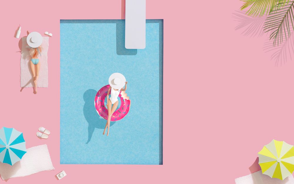 Barbie-like doll in donut ring in pool, with friend at poolside with parasols and towels