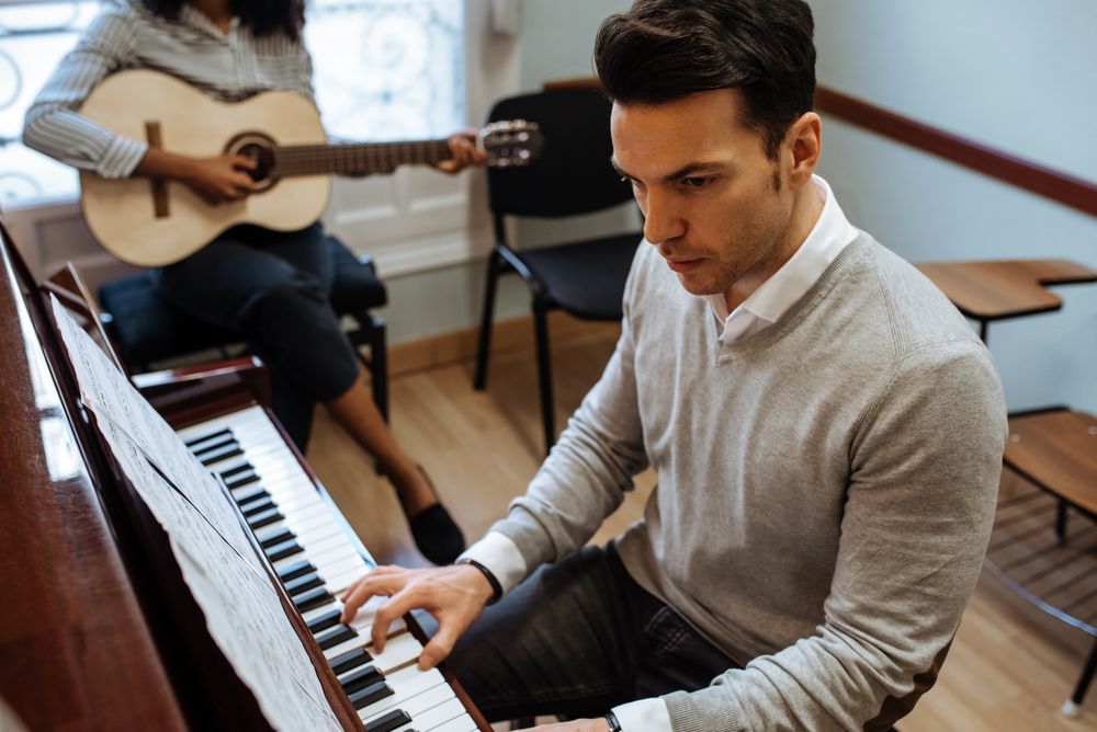 Man playing piano near woman playing guitar in studio
