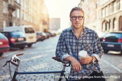 Man in glasses on cobble street leaning on bike 5QorGb