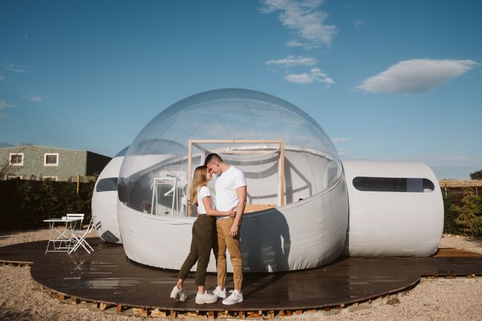 Affectionate couple kissing near bubble hotel