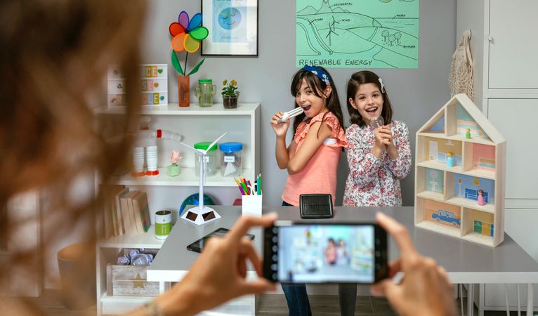 Teacher recording video in mobile phone of happy students singing using light bulbs as microphones