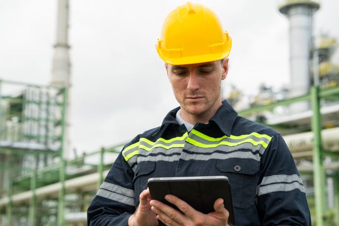 Refinery oil engineer worker in protection hardhat with digital tablet inspecting at petrochemical factory.