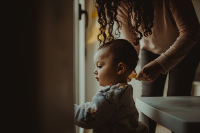 Toddler looking out the window with mother standing behind him