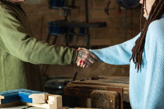 Woman greeting woodworker with handshake in workshop