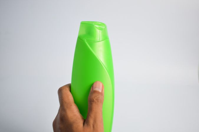 Hand holding mockup green shampoo bottle