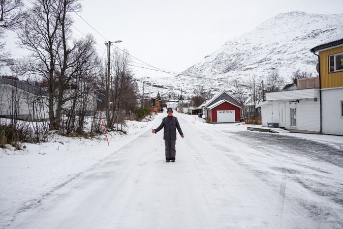 Solitary old man on empty street in small town against snowy hillside