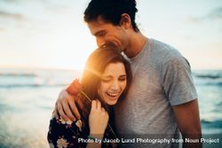 Man hugging his girlfriend holding a rose at the beach 5rloPb