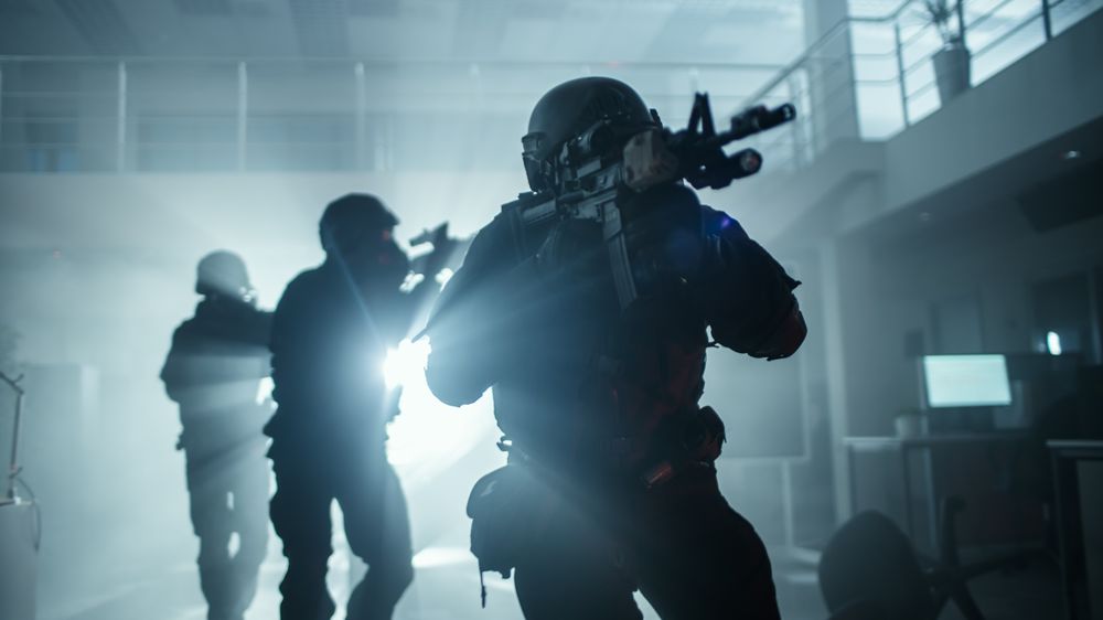 Masked Squad of Armed SWAT Police Officers Move in a Hall of a Dark Seized Office Building with Desks and Computers.