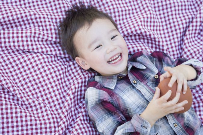 Happy Biracial Boy Playing with Football on Picnic Blanket