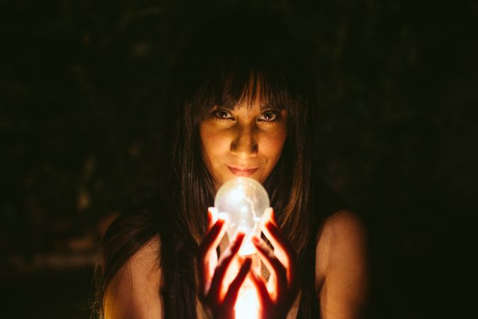Thoughtful woman with burning lightbulb in darkness