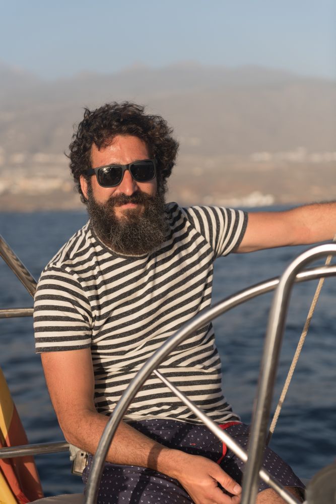 Smiling man holding steering wheel on yacht on water near quay