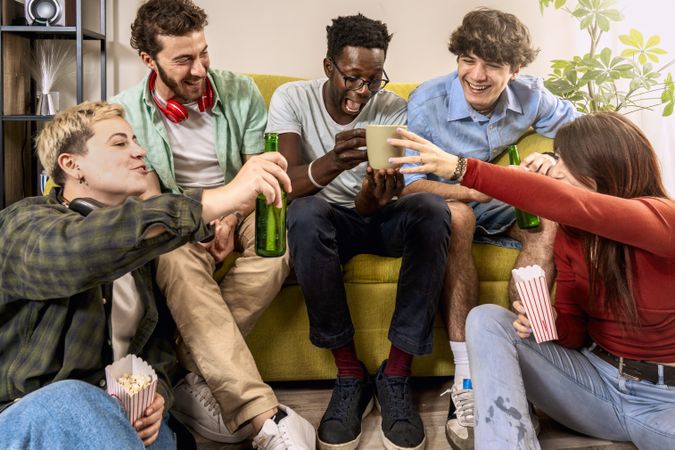 Five multicultural friends sharing coffee and popcorn snacks in a cheerful living room gathering