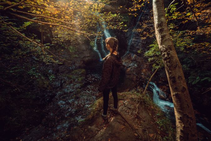 woman standing in a Small river and waterfall flowing in green dark beautiful forest.