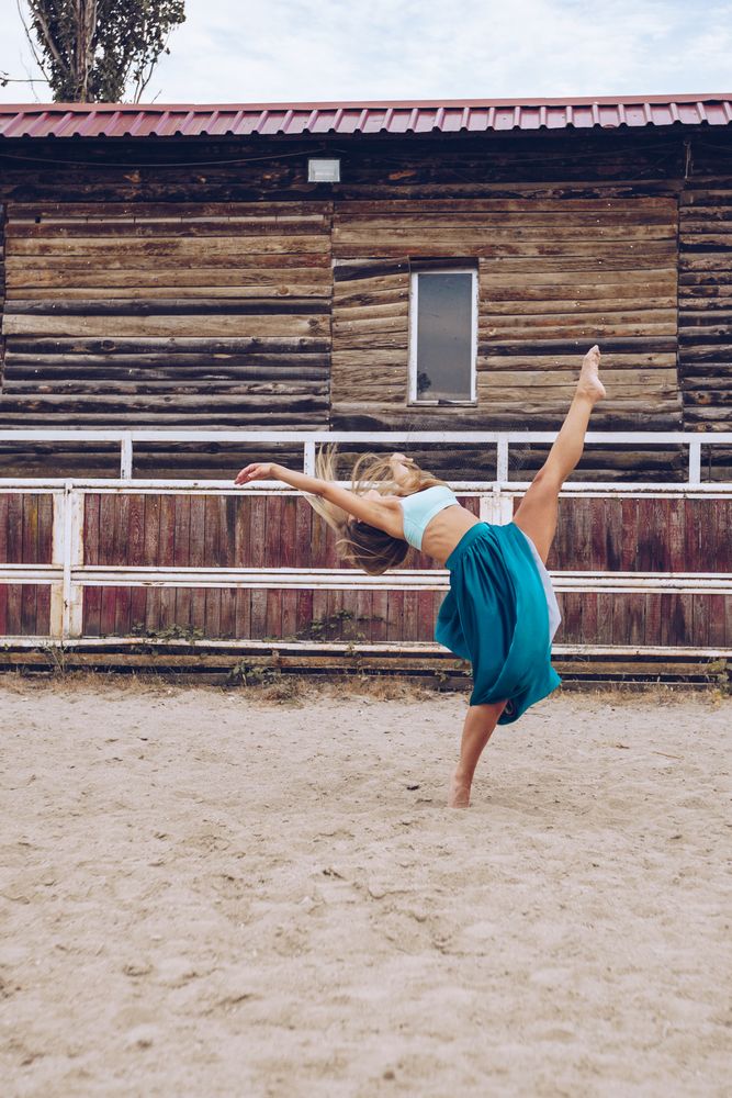 Flexible woman in colorful skirt dancing at rural paddock