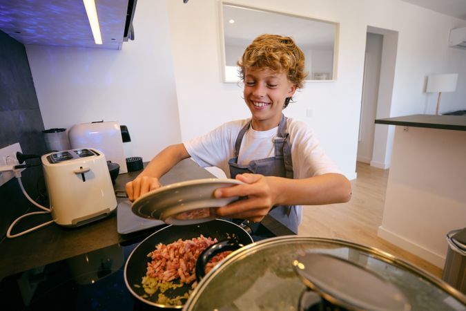 Smiling boy putting cut bacon in pan while cooking