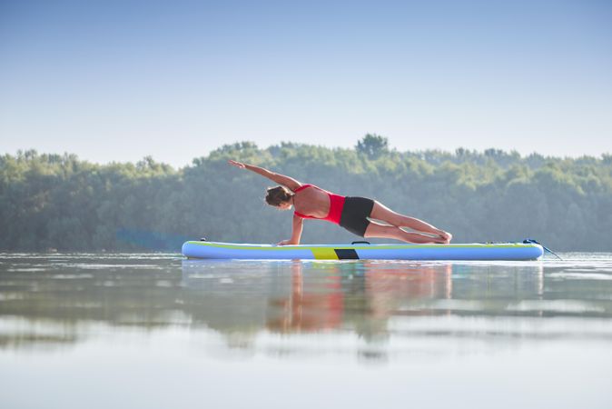 Woman doing side planks on paddleboard in lake