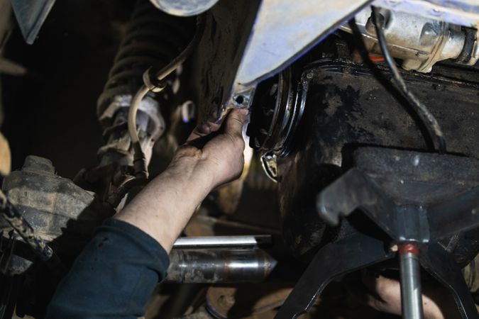 Anonymous adult repairman fixing car detail raised on lift in garage