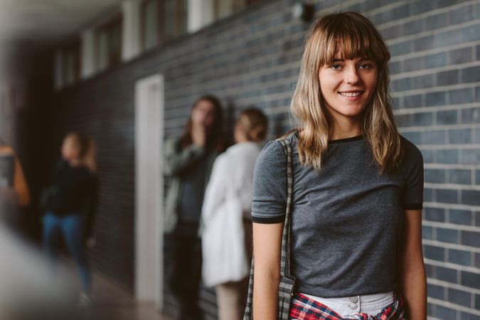 Portrait of beautiful young woman walking in college corridor with students standing in background