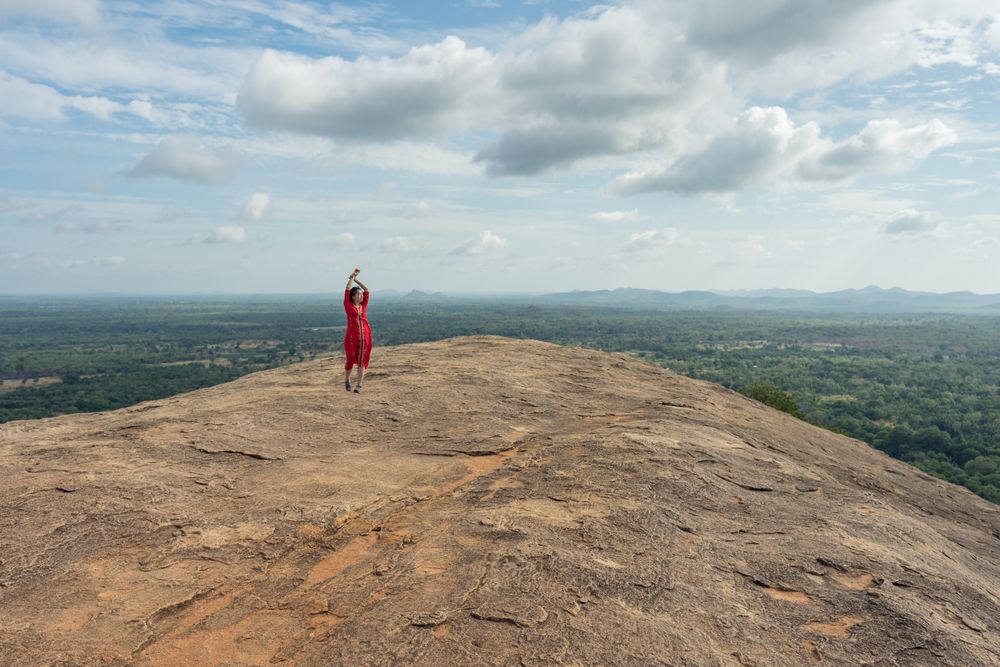 Tourist against solitary rock in middle of green forested plain under clear sky in summer