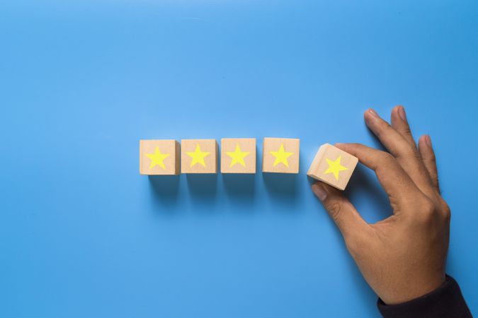 male hand put wooden blocks with five stars isolated on blue background.