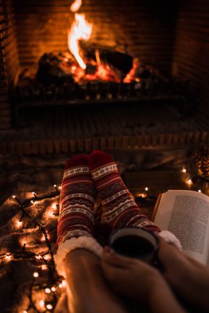 Faceless woman sitting by fireplace and holding mug