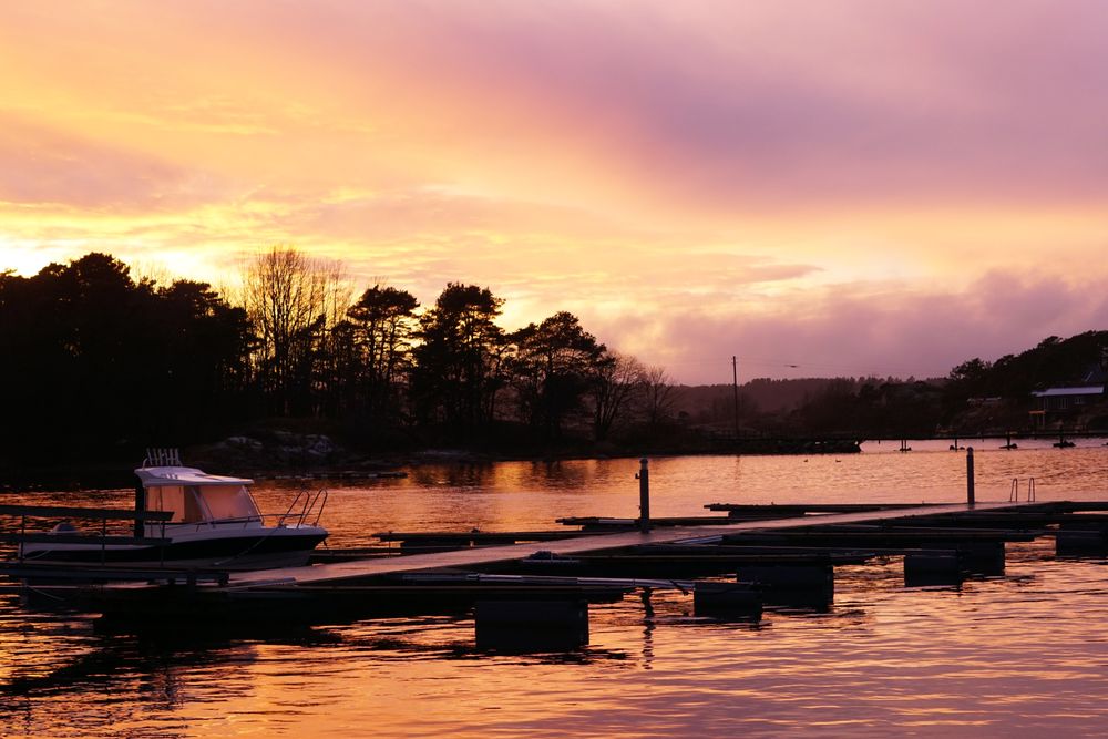 Boat by pier in twilight and distant forest silhouette