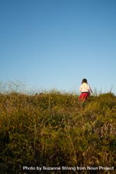 Back view of young girl in pink skirt climbing up a grassy hill 4d8qD4