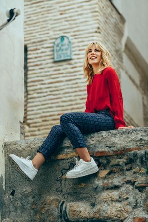 Smiling blond woman in red sweater sitting on stone wall