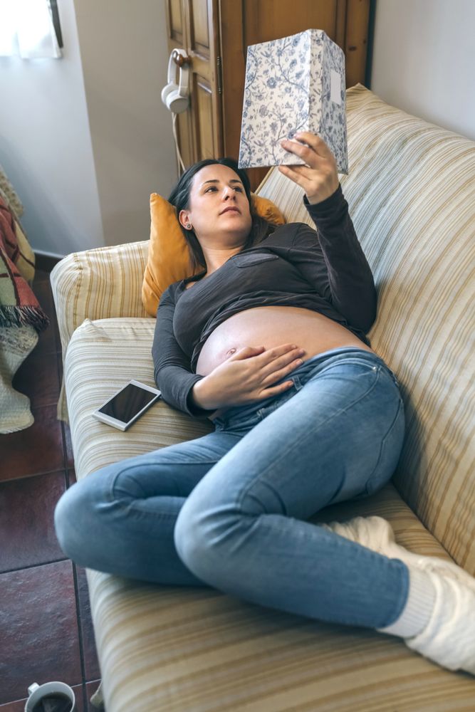 Pregnant woman reading a book lying on the couch