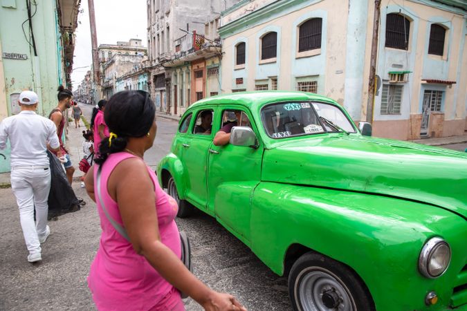 People walking down the street beside a green vintage car in Havana, Cuba