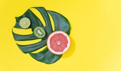 Monstera leaf with red grapefruit, lime and kiwi on bright yellow background