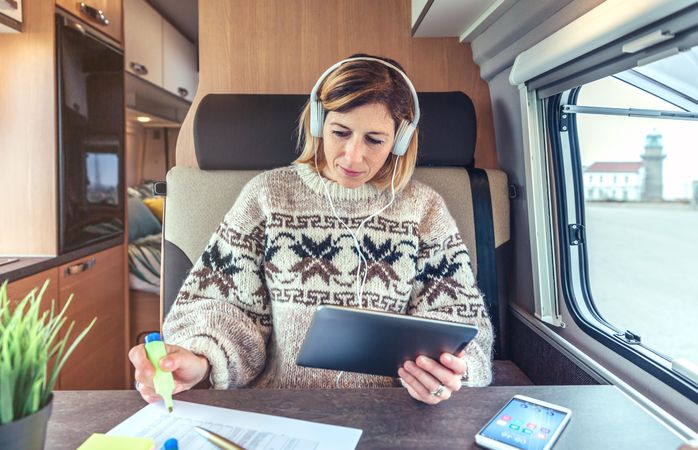 Female sitting in back of camper van working on digital tablet with headphones