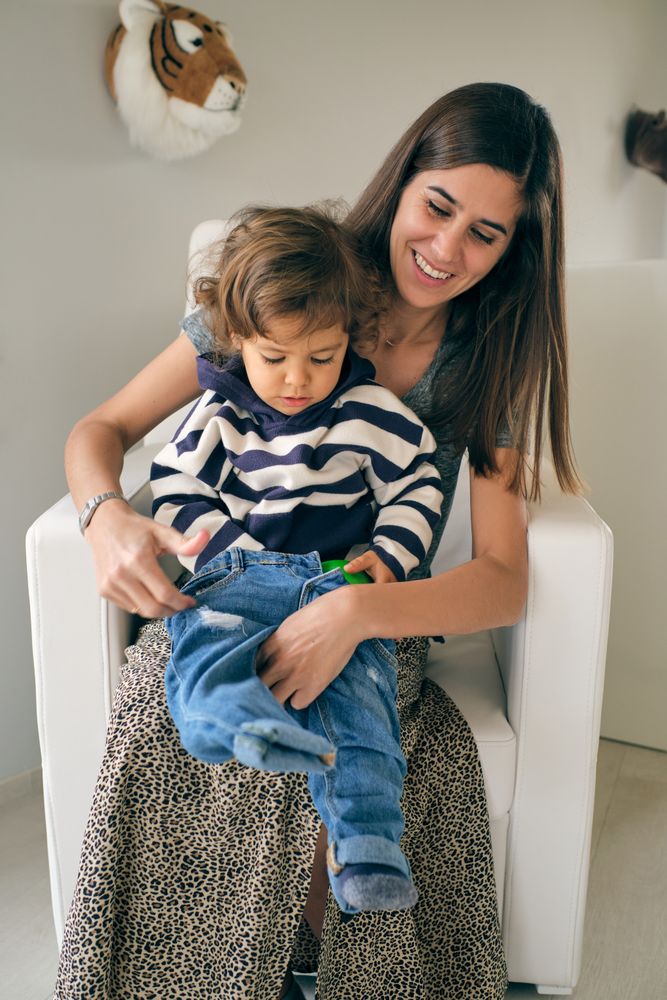 Happy mother putting jeans on son