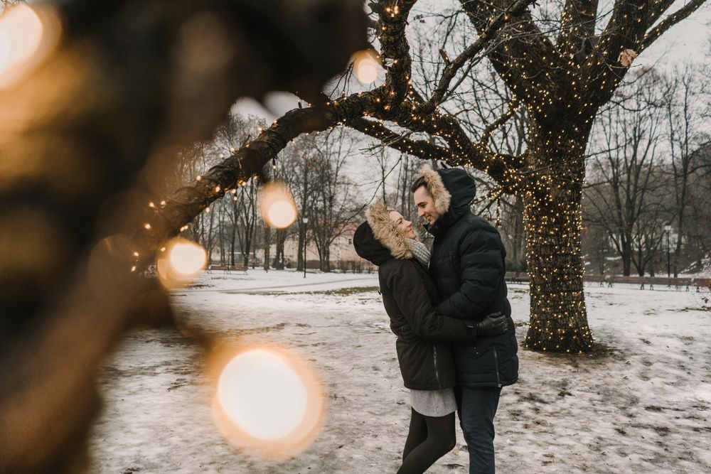 Smiling couple having fun on street near tree with fairy lights