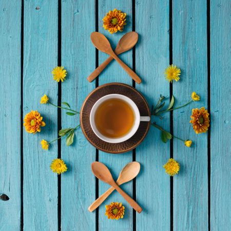 Orange and yellow floral pattern arranged around cup of tea on blue background