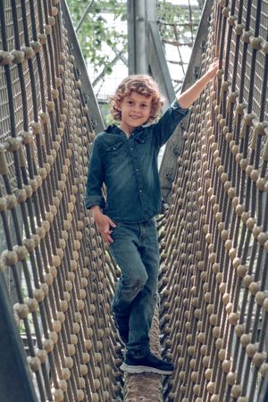 Cheerful adorable boy passing route in rope park