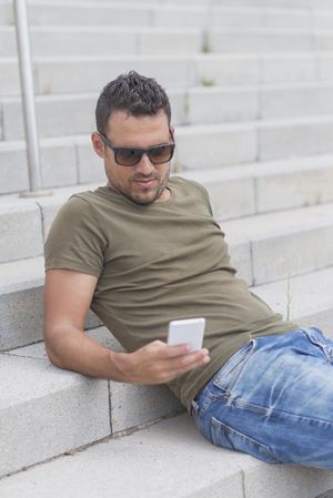 Man sitting on outdoor stairs while texting on phone, vertical